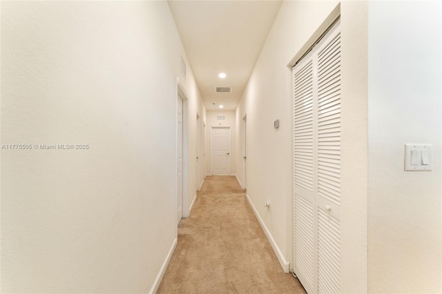 hallway featuring baseboards, visible vents, and light colored carpet