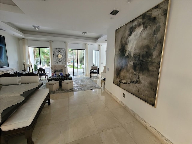 corridor with baseboards, visible vents, light tile patterned floors, and a raised ceiling