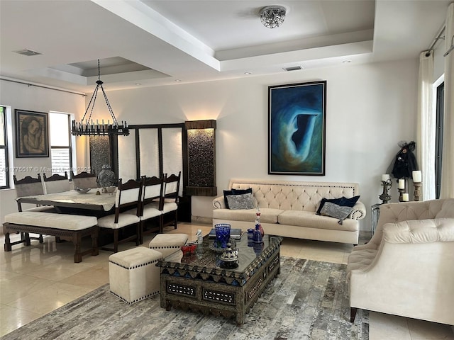 living area with visible vents, a notable chandelier, tile patterned flooring, and a raised ceiling
