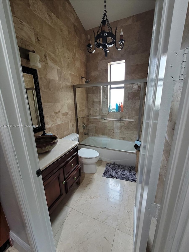 bathroom featuring combined bath / shower with glass door, toilet, vanity, tile walls, and an inviting chandelier