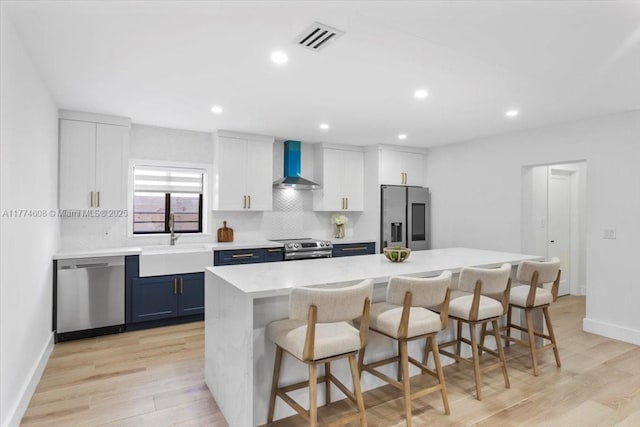 kitchen with wall chimney range hood, a kitchen breakfast bar, a sink, light wood-style floors, and appliances with stainless steel finishes