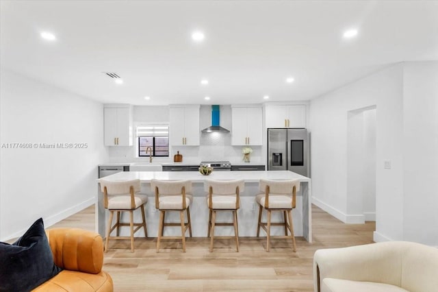 kitchen featuring wall chimney exhaust hood, stainless steel appliances, open floor plan, a breakfast bar, and a kitchen island