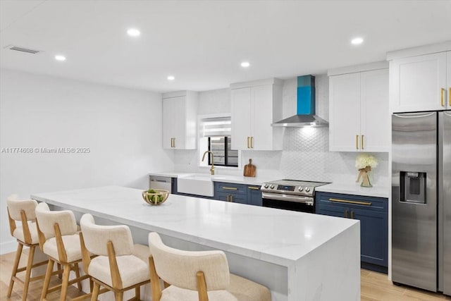 kitchen with blue cabinetry, wall chimney exhaust hood, appliances with stainless steel finishes, and a sink
