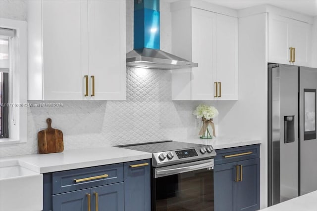 kitchen with wall chimney exhaust hood, blue cabinets, white cabinetry, light countertops, and appliances with stainless steel finishes