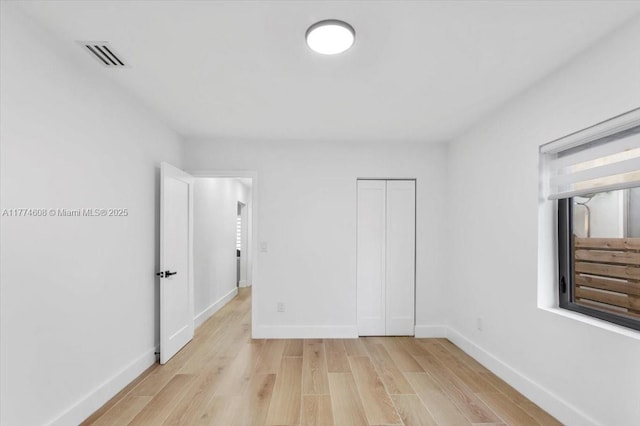 unfurnished bedroom with baseboards, a closet, visible vents, and light wood-style flooring