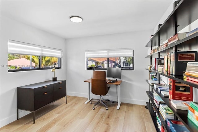 home office with light wood-style floors, a healthy amount of sunlight, and baseboards