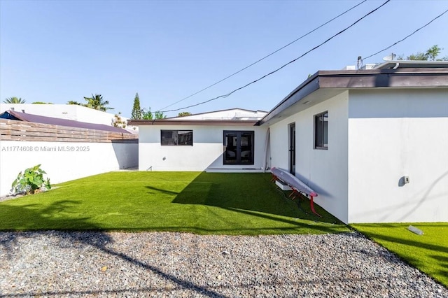 rear view of house with fence, a lawn, french doors, and stucco siding