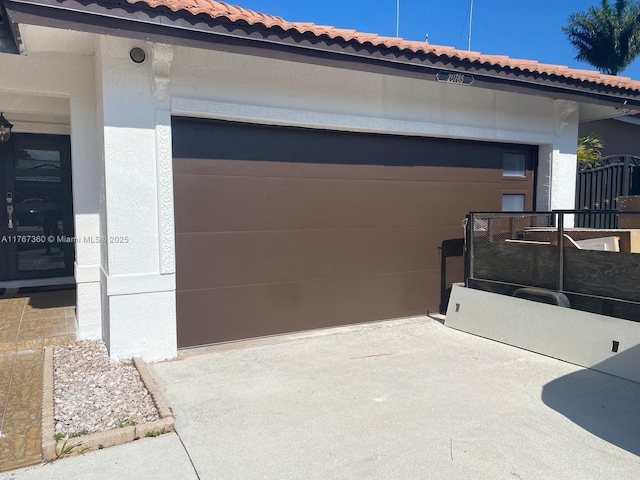 view of side of property featuring concrete driveway, stucco siding, a tile roof, and a garage