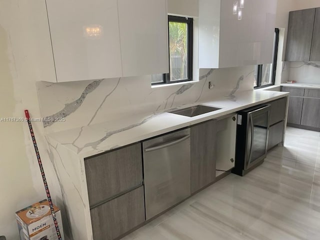 kitchen featuring modern cabinets, light stone counters, dishwasher, a sink, and backsplash