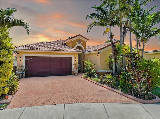 mediterranean / spanish-style house with a tile roof, stucco siding, a garage, and decorative driveway