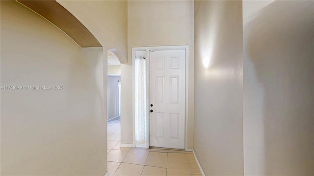 hall with light tile patterned floors, baseboards, and arched walkways