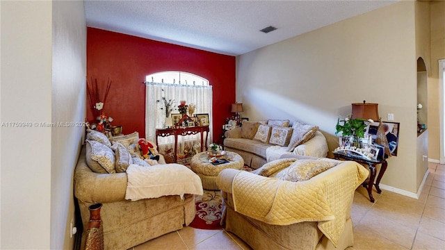 living area featuring a textured ceiling, light tile patterned floors, visible vents, an accent wall, and arched walkways