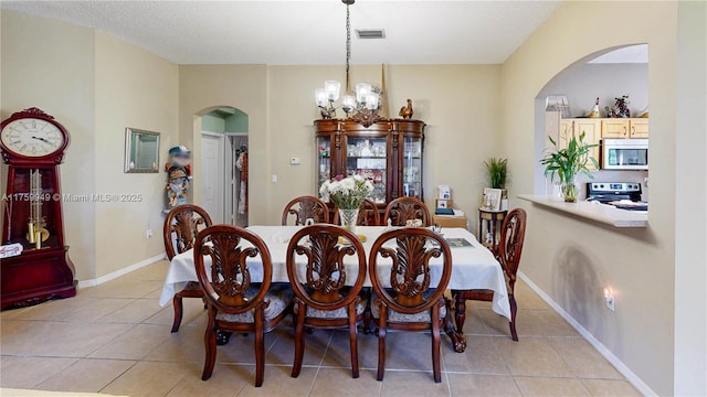 dining area featuring arched walkways, an inviting chandelier, light tile patterned floors, and visible vents