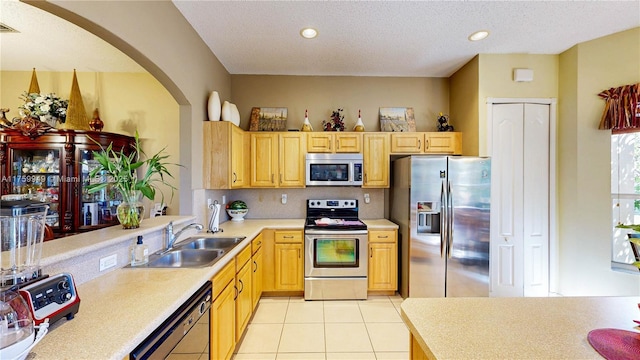 kitchen featuring a sink, light countertops, light brown cabinetry, arched walkways, and appliances with stainless steel finishes