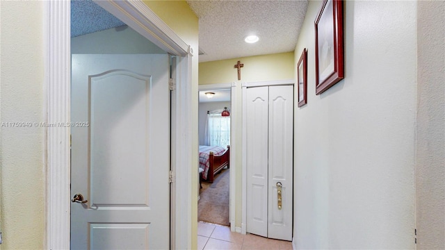 hallway with a textured ceiling and light tile patterned floors
