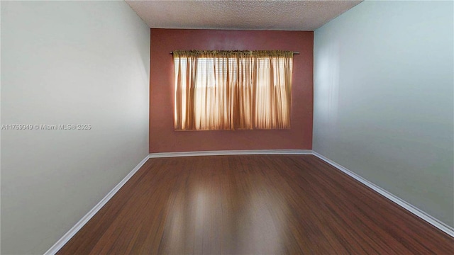 empty room with a textured ceiling, baseboards, and wood finished floors