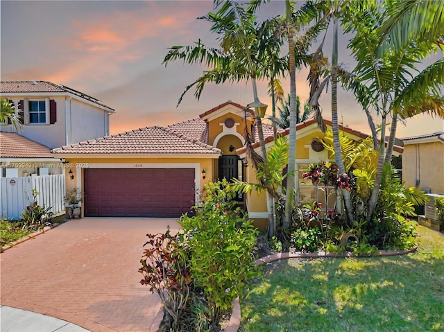 mediterranean / spanish-style home with a tile roof, a garage, stucco siding, and decorative driveway