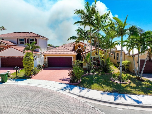 mediterranean / spanish-style house featuring an attached garage, a tiled roof, stucco siding, fence, and decorative driveway