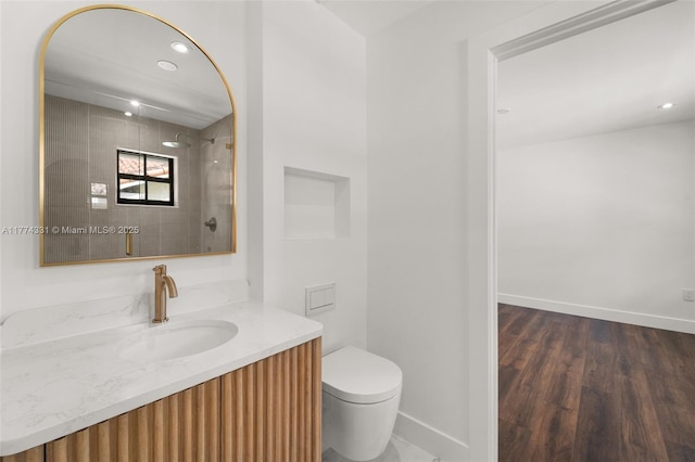 full bathroom with vanity, baseboards, toilet, tiled shower, and wood finished floors