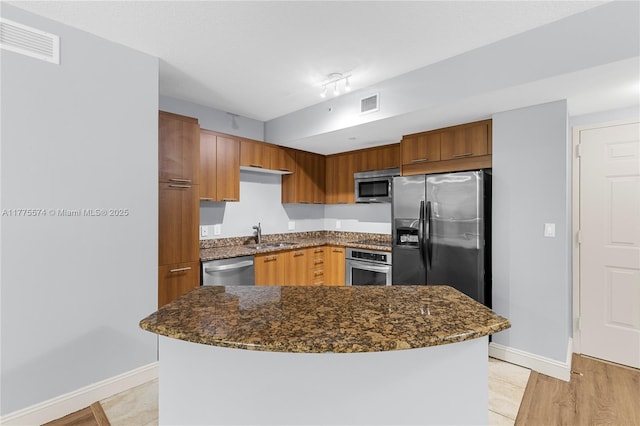 kitchen featuring stainless steel appliances, a sink, baseboards, and dark stone counters