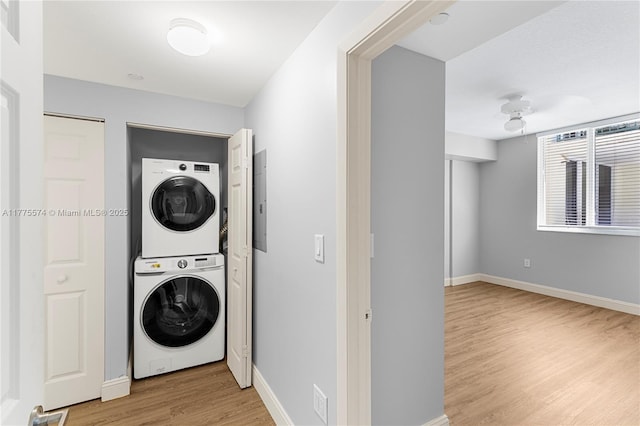 laundry area featuring stacked washer / drying machine, light wood finished floors, and baseboards