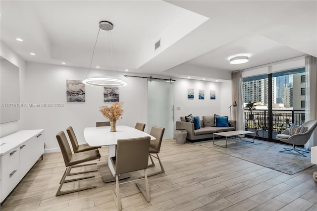 dining area with recessed lighting, a raised ceiling, a barn door, visible vents, and light wood-style flooring