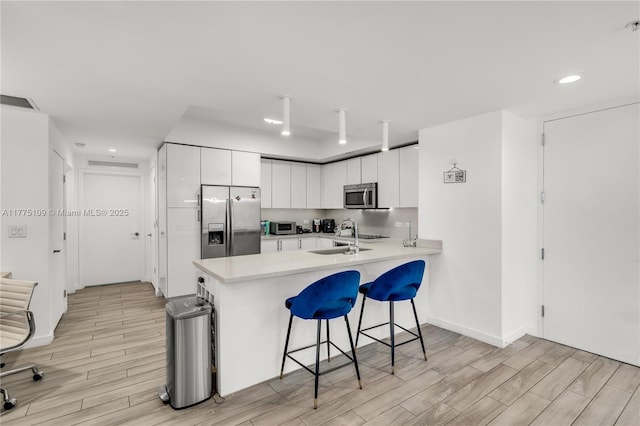 kitchen featuring light countertops, a sink, a breakfast bar area, a peninsula, and stainless steel appliances