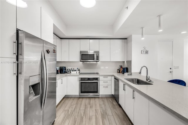 kitchen with a sink, white cabinetry, light countertops, and appliances with stainless steel finishes