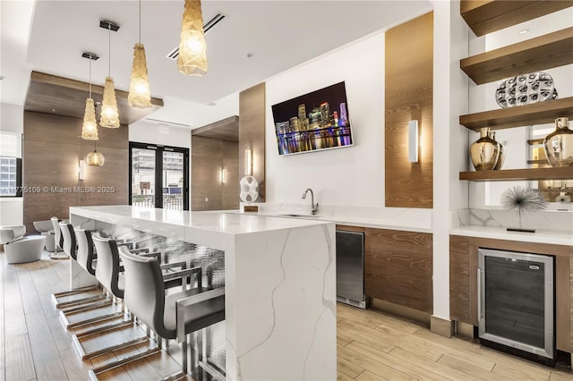 bar with light wood-style flooring, wine cooler, a sink, decorative light fixtures, and fridge
