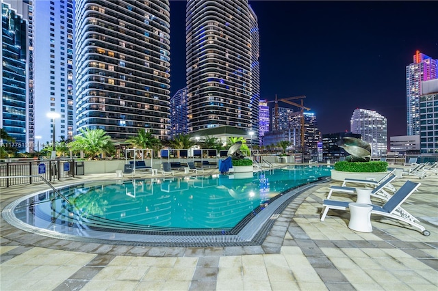 pool at twilight featuring a view of city lights, a community pool, and a patio area