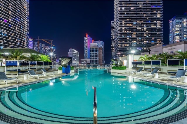 pool at night featuring a patio area, a view of city lights, and a community pool