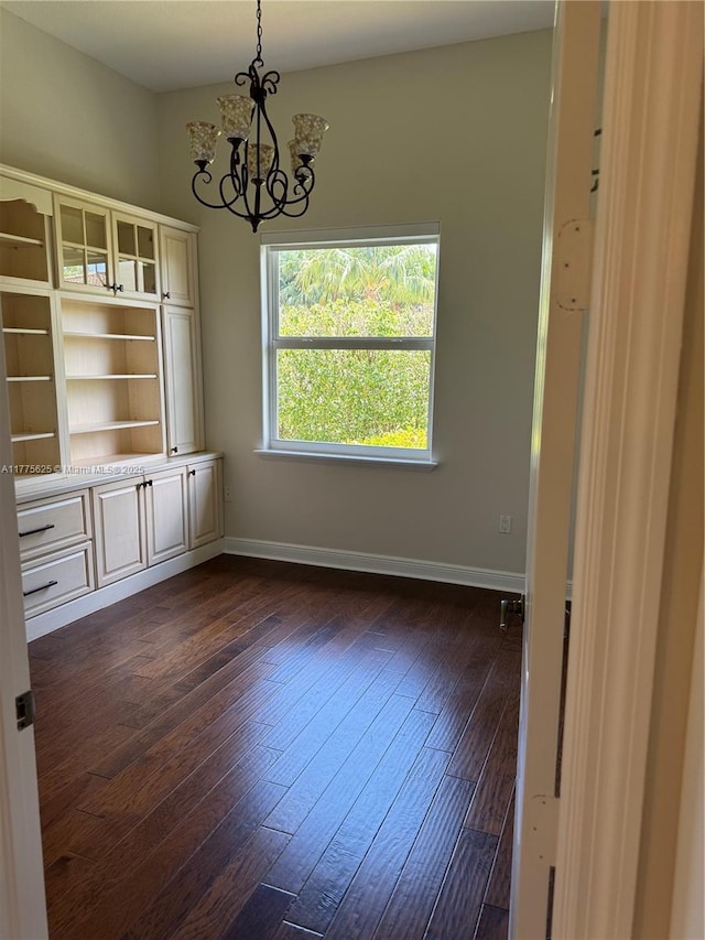 unfurnished dining area with a chandelier, dark wood-type flooring, and baseboards
