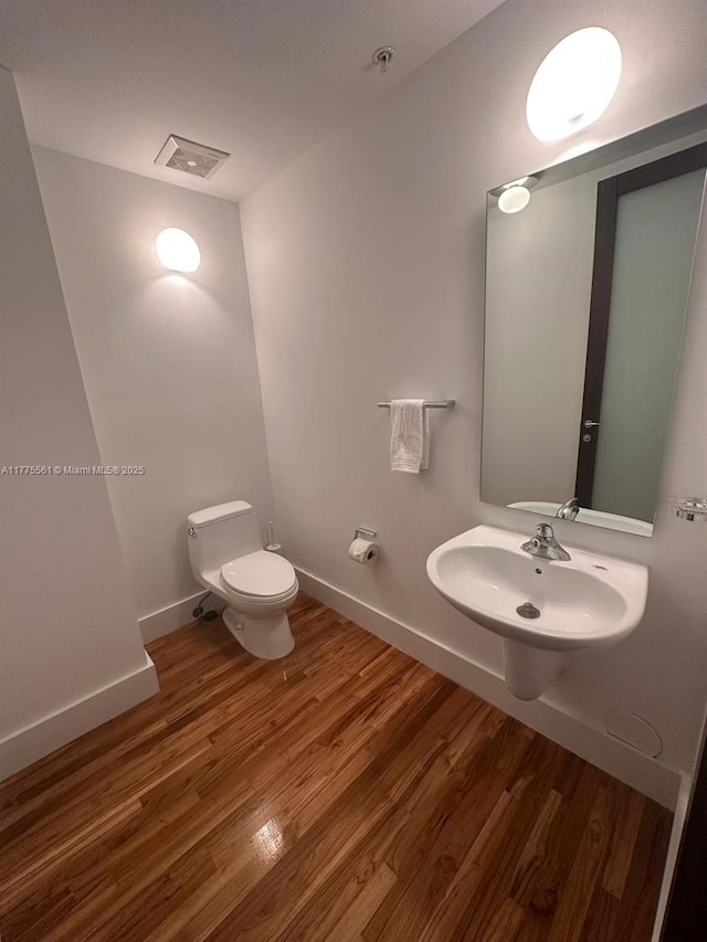 half bathroom with toilet, visible vents, a sink, and wood finished floors