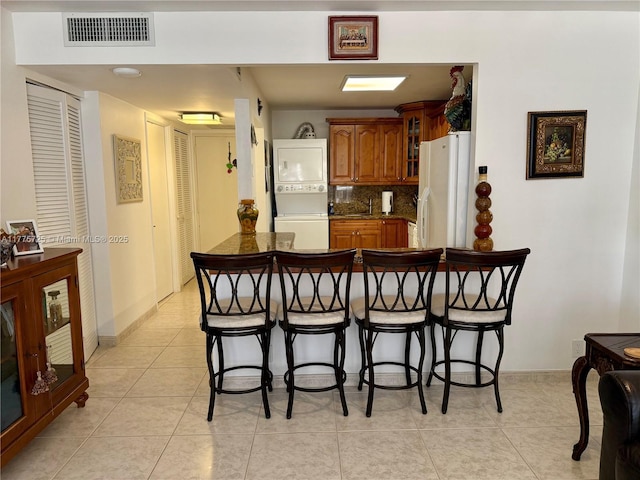 1901 Brickell Ave Unit B804, Miami, FL 33129 - kitchen with brown cabinetry, visible vents, stacked washer / drying machine, freestanding refrigerator, and a breakfast bar