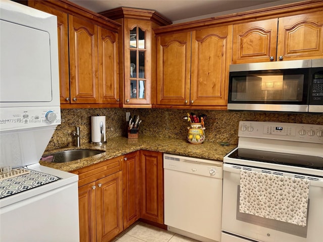 1901 Brickell Ave Unit B804, Miami, FL 33129 - kitchen featuring white appliances, stacked washing machine and dryer, dark stone countertops, glass insert cabinets, and brown cabinetry