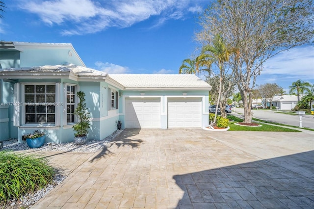 view of side of home featuring decorative driveway, stucco siding, a garage, and a tiled roof