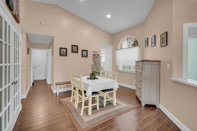 dining room featuring dark wood-style floors, baseboards, and high vaulted ceiling