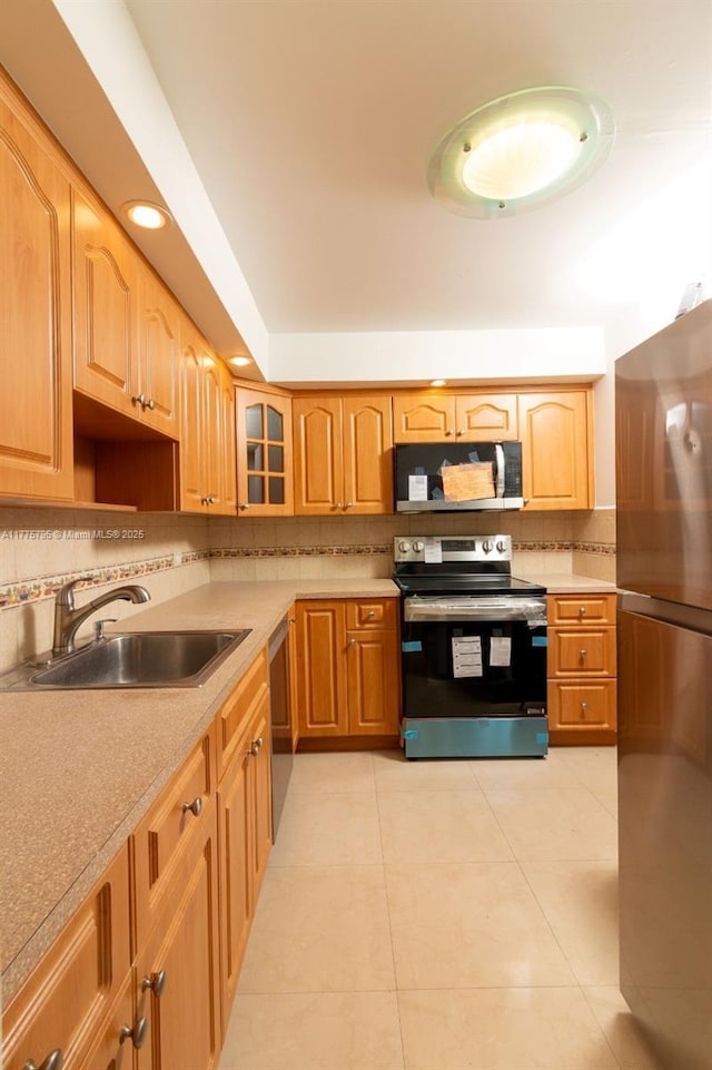 447 NE 195th St Unit 217, Miami, FL 33179 - kitchen featuring appliances with stainless steel finishes, a sink, tasteful backsplash, light tile patterned floors, and glass insert cabinets