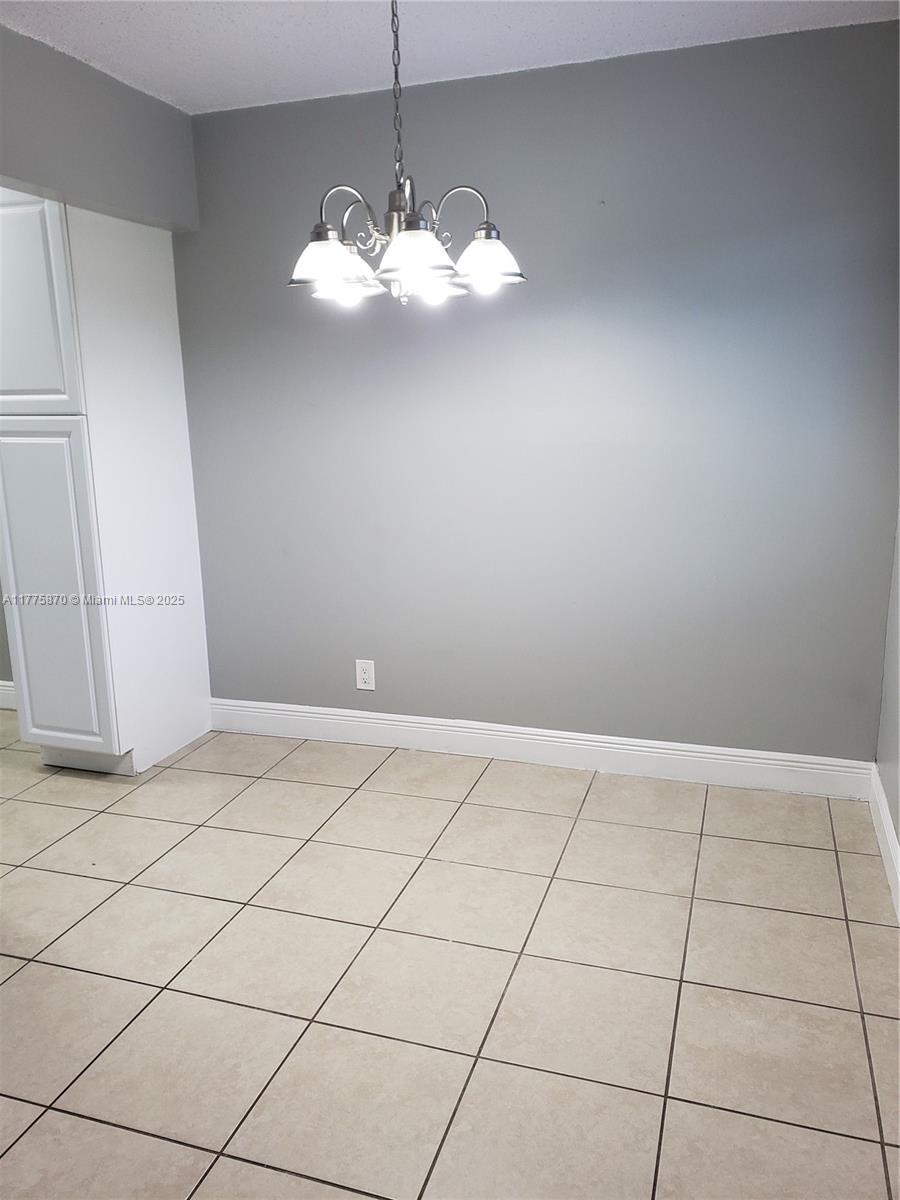 unfurnished room with baseboards, a notable chandelier, and light tile patterned floors