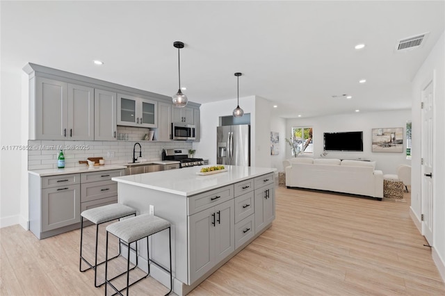 kitchen with visible vents, light wood-style floors, appliances with stainless steel finishes, gray cabinets, and a breakfast bar area