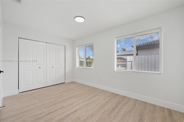unfurnished bedroom featuring baseboards, a closet, and light wood-style flooring
