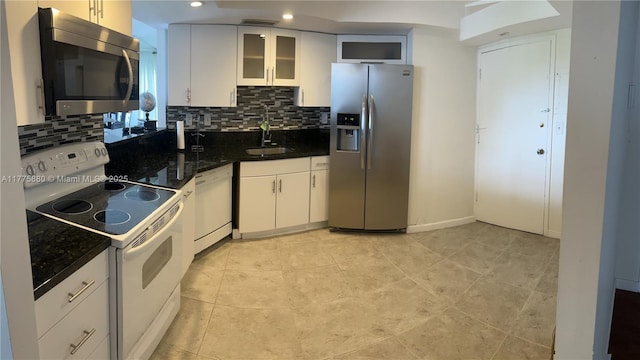 kitchen with a sink, decorative backsplash, glass insert cabinets, stainless steel appliances, and white cabinetry