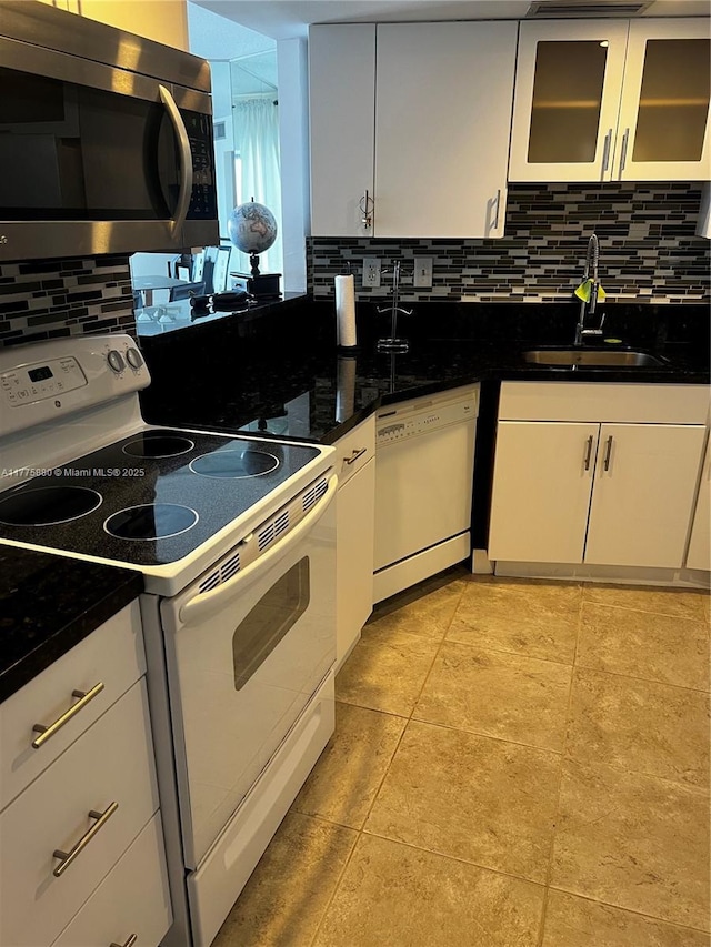 kitchen featuring dark countertops, a sink, white appliances, backsplash, and white cabinetry