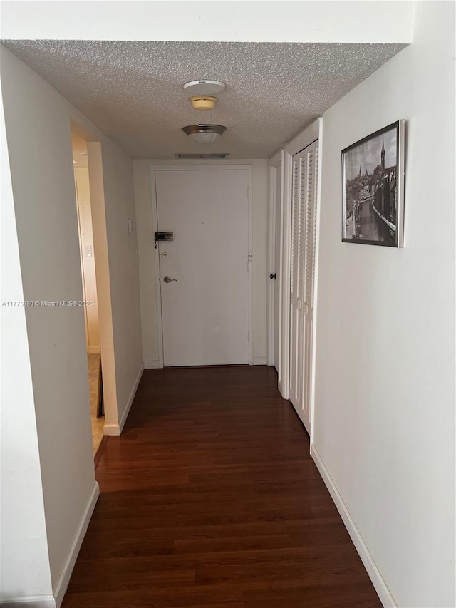 hall with dark wood finished floors, baseboards, and a textured ceiling