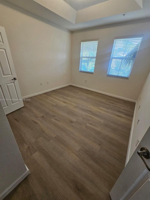 unfurnished room featuring baseboards, a raised ceiling, and dark wood-style flooring