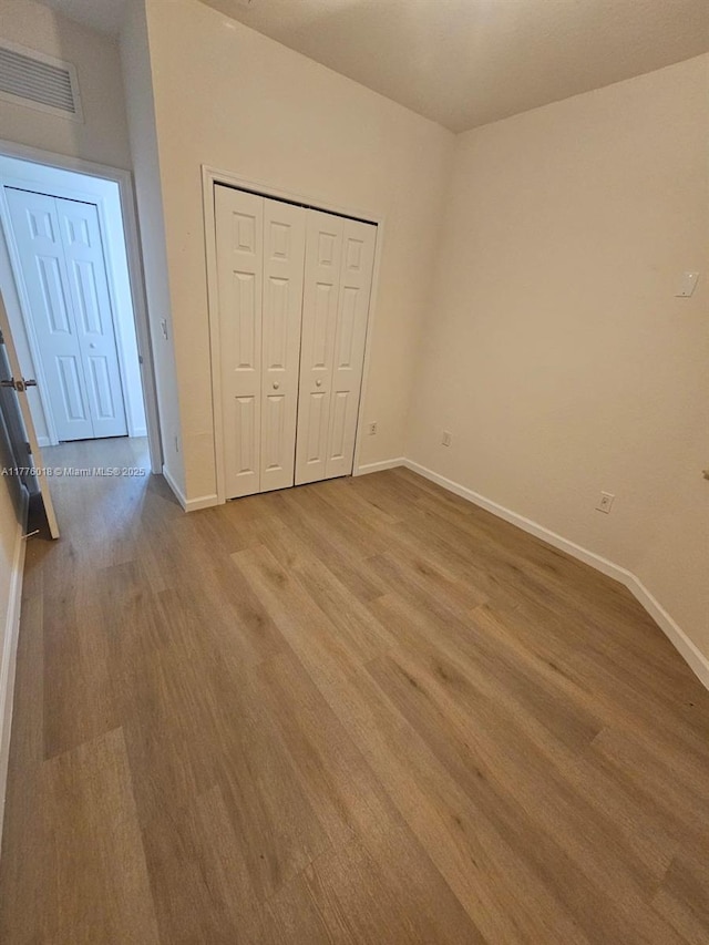 unfurnished bedroom featuring light wood finished floors, baseboards, visible vents, and a closet