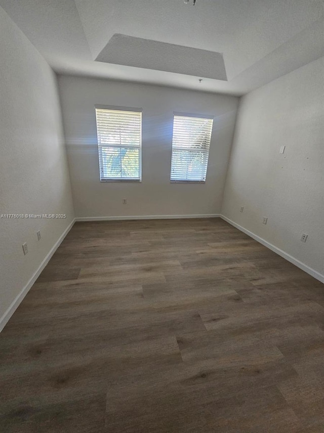 unfurnished room featuring baseboards, dark wood-style flooring, and a raised ceiling