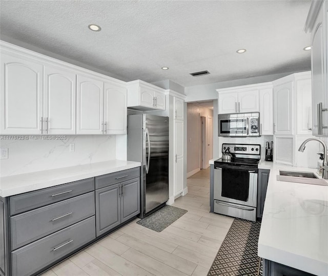 217 SE 5th St, Dania Beach, FL 33004 - kitchen with stainless steel appliances, gray cabinetry, a sink, white cabinetry, and decorative backsplash