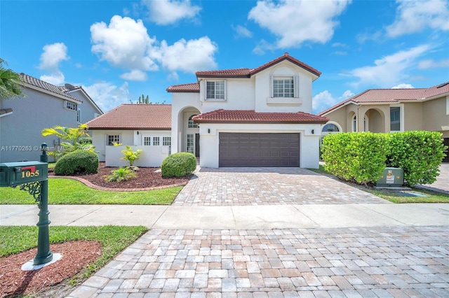 mediterranean / spanish-style house featuring decorative driveway, an attached garage, a tile roof, and stucco siding