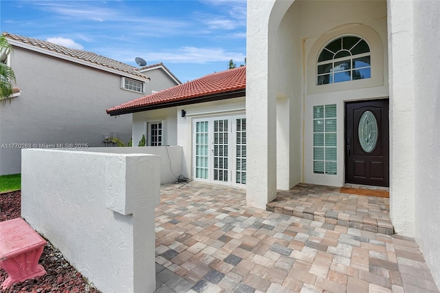 property entrance with stucco siding, a patio area, and a tiled roof
